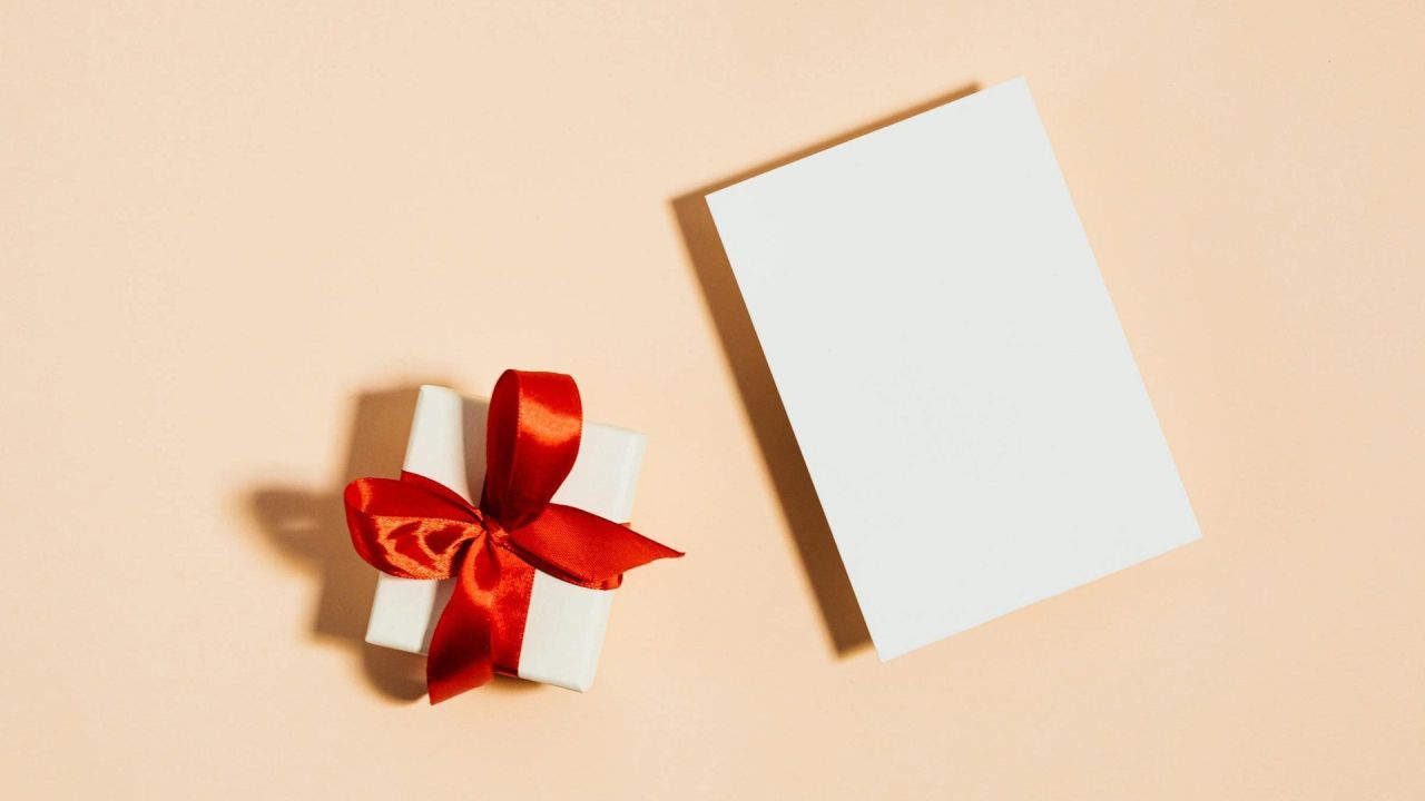 Pacchetto regalo bianco con fiocco rosso e cartolina bianca su sfondo color pesca, carta regalo come idea regalo