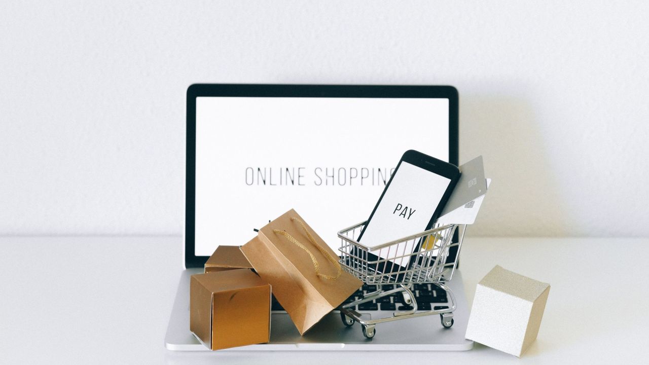 Laptop con scritta Online Shopping, smartphone Pay nel carrello e pacchi acquisti